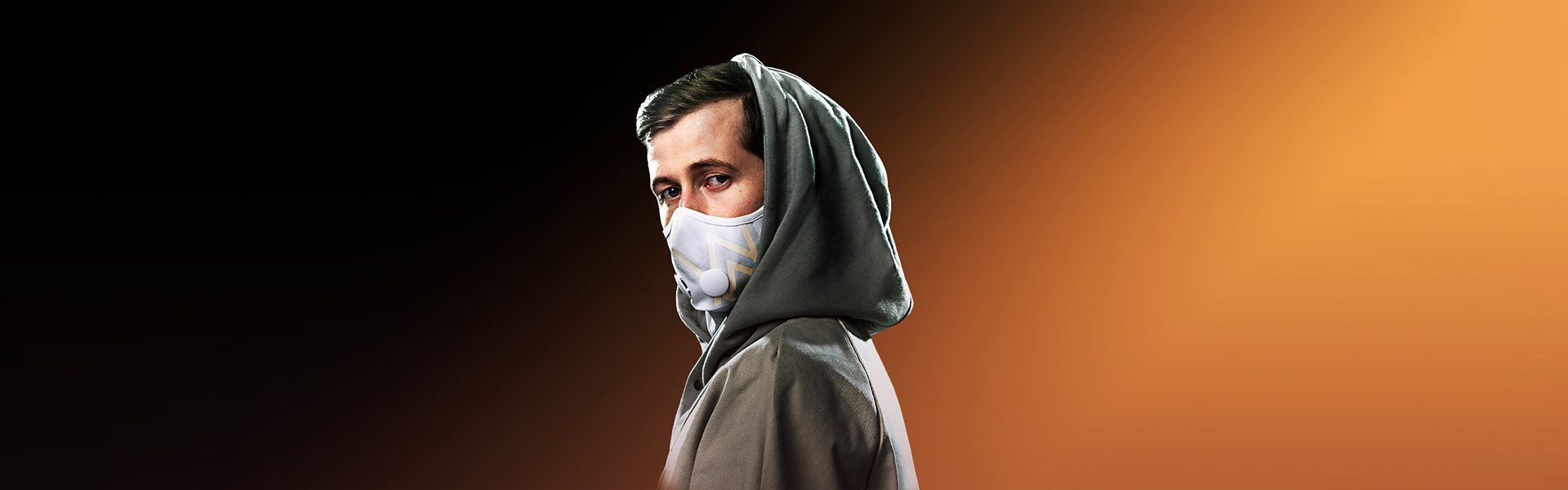 Alan Walker in his signature grey hoodie and mask against a warm amber background, official artist press photograph