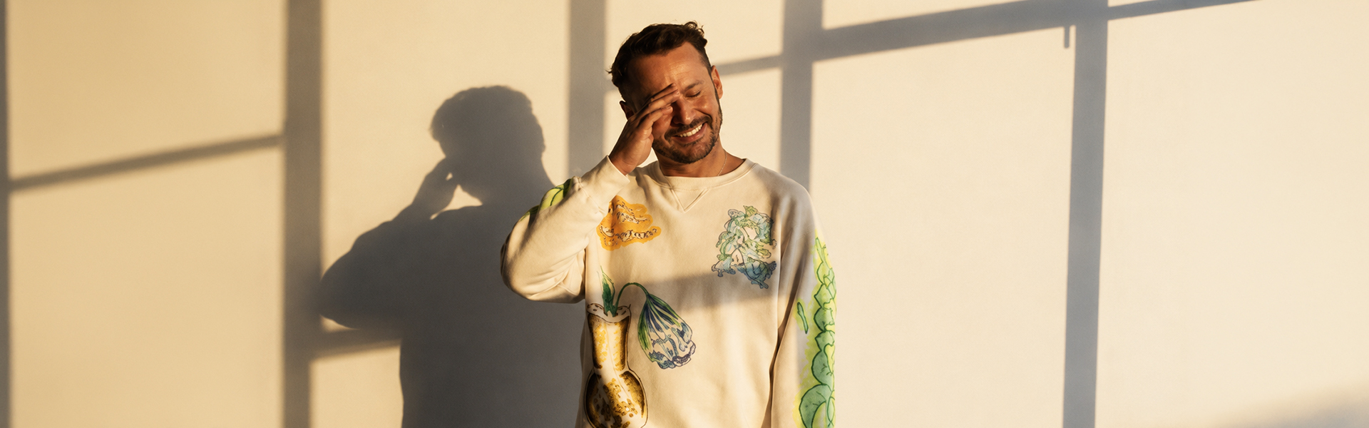 Ben Howard smiling in a white graphic sweatshirt in a sunlit room for his India debut tour 2024