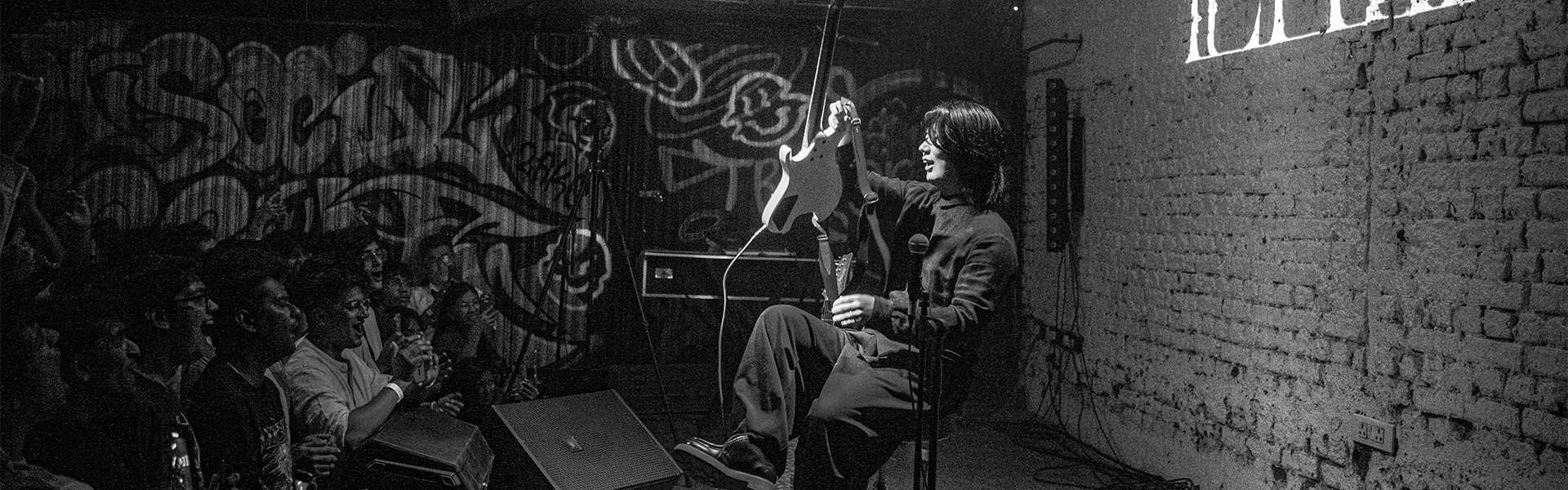 Ichika Nito seated playing guitar on stage at an intimate India debut show in 2025 with audience close by